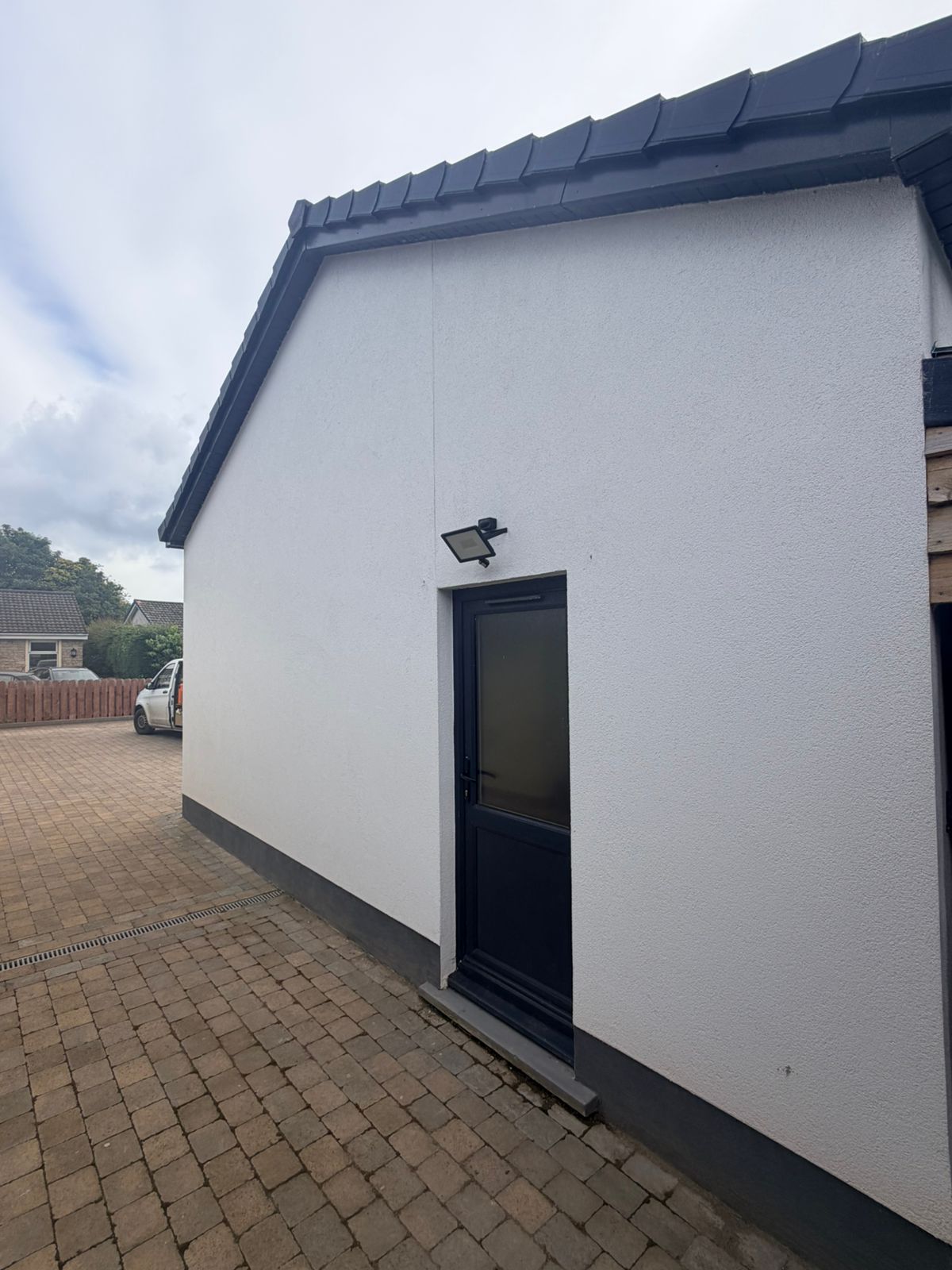 Side elevation of the completed detached triple garage showing the rendered gable, tiled roof verge and a separate personnel access door, Isle of Man